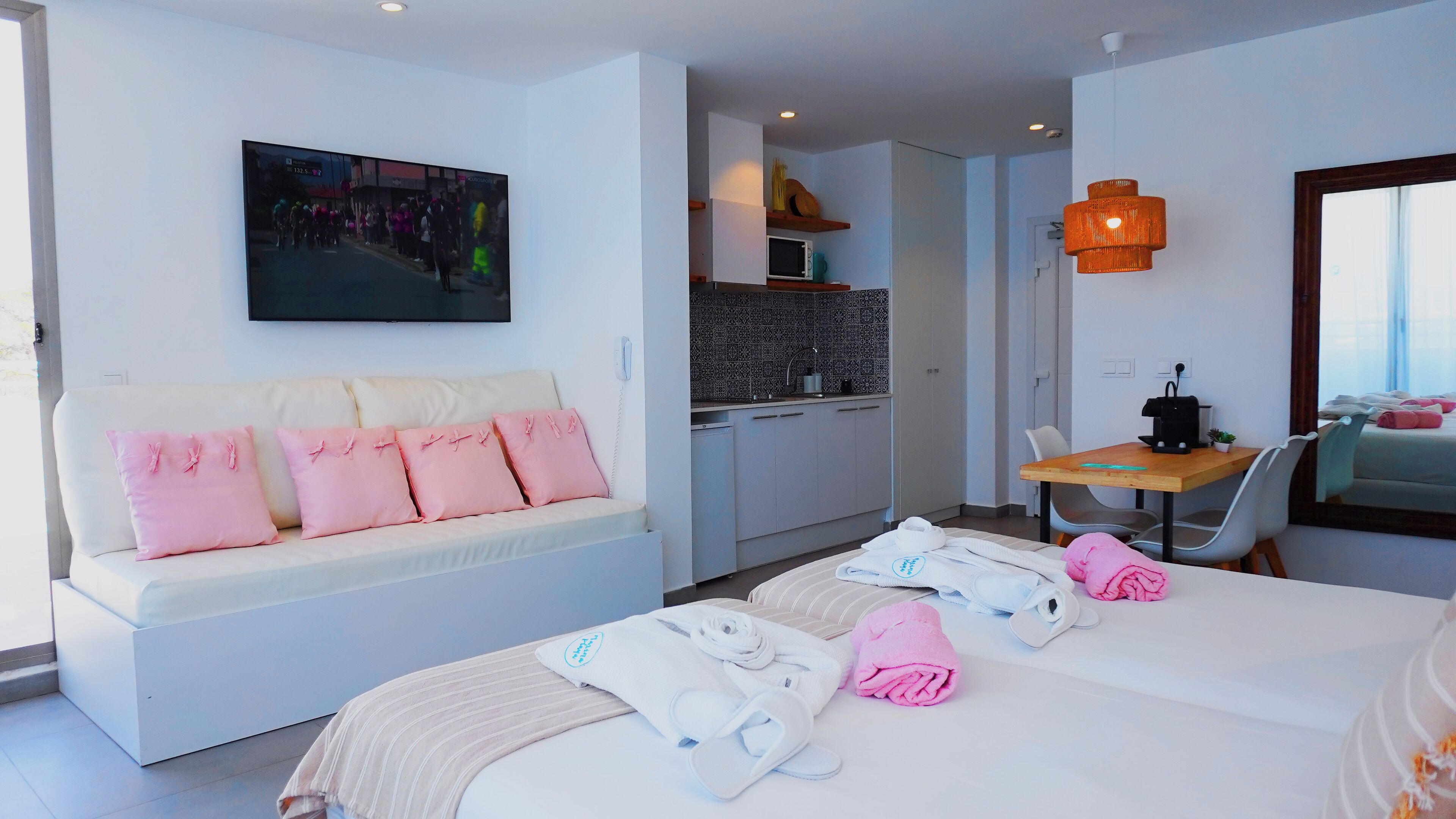 A hotel room with a sofa, a bed with towels, a dining area, and a kitchen.