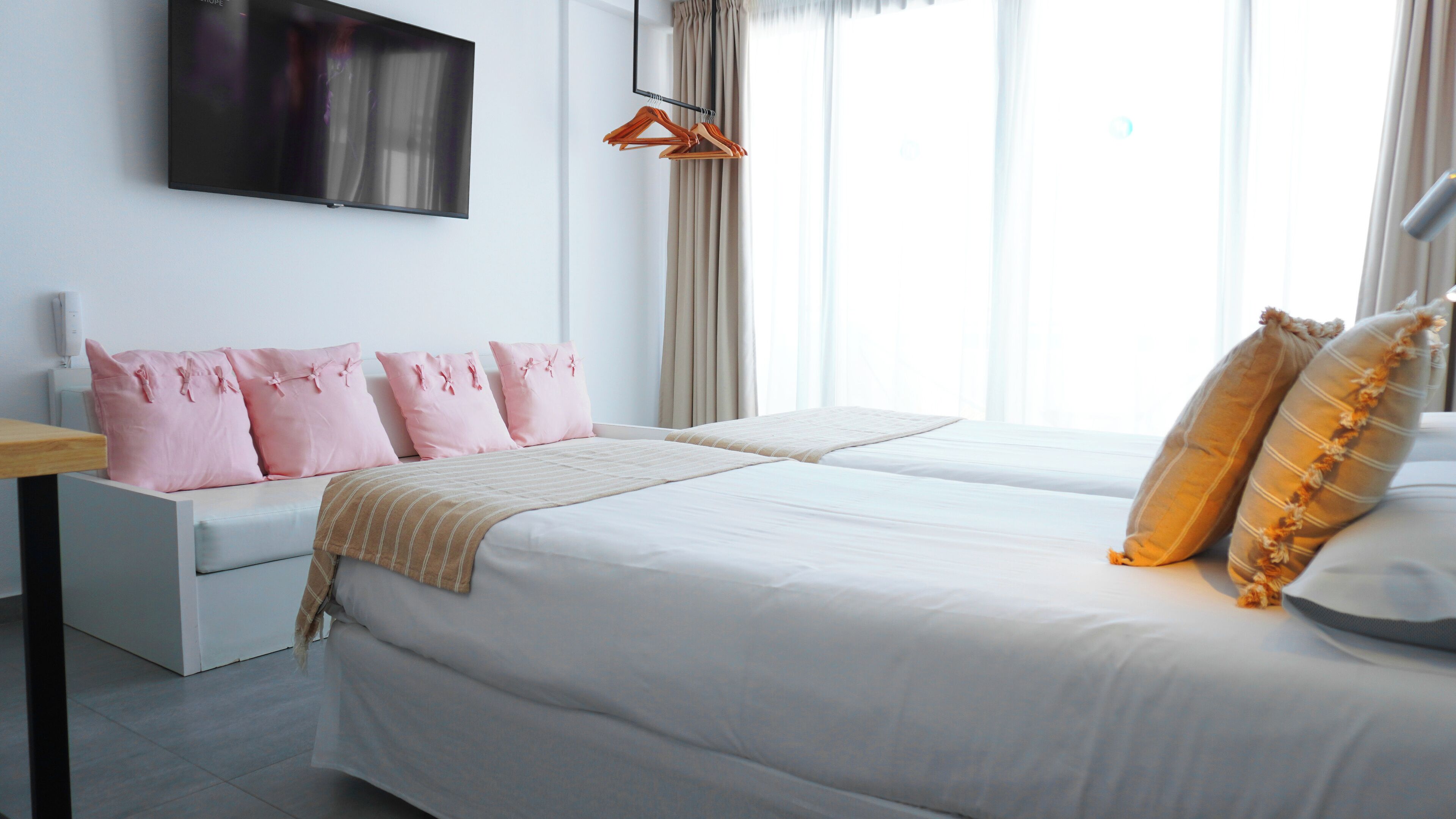 A hotel room with a bed, a sofa, a TV, and a window with curtains.