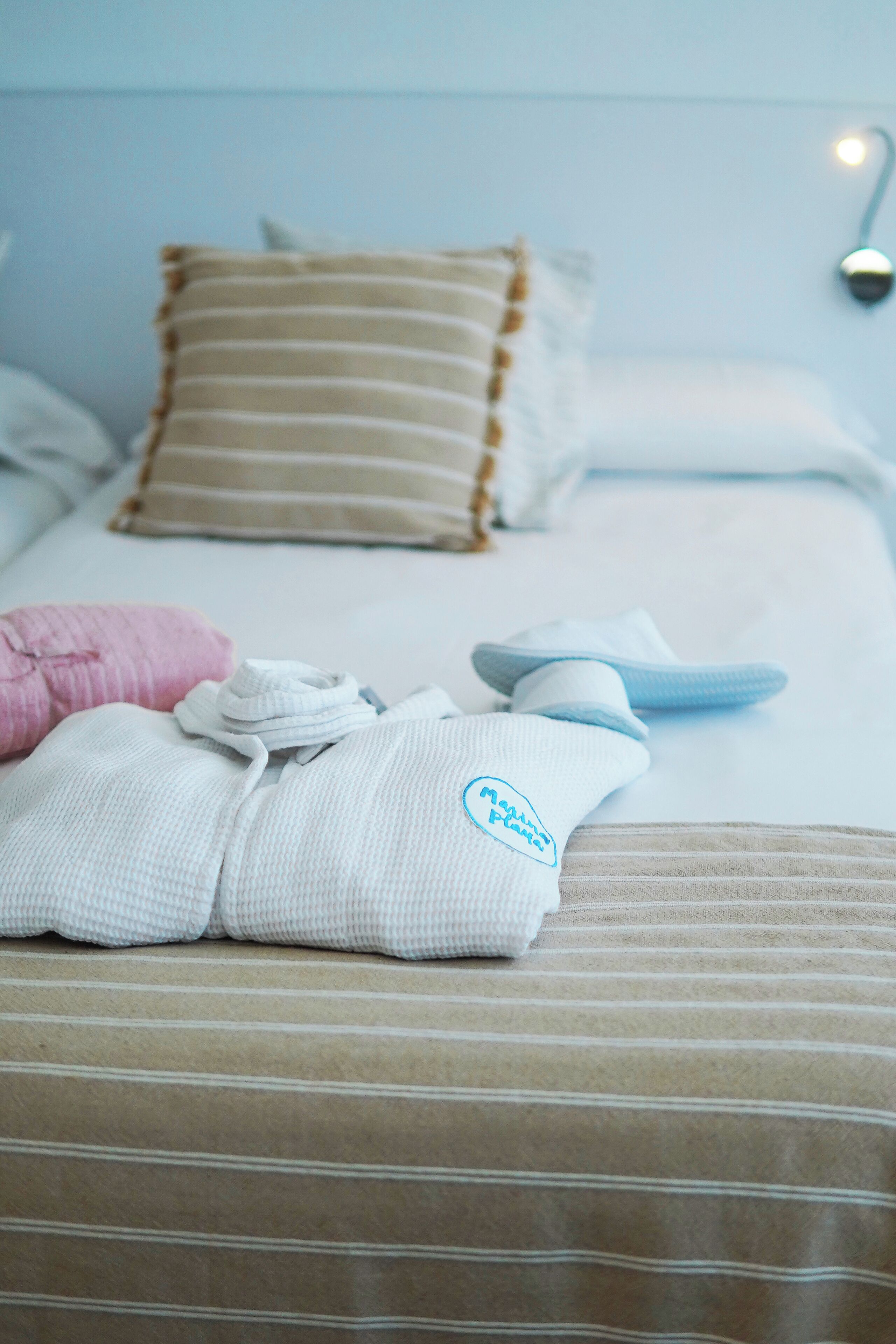 Una cama bien tendida con almohadones a rayas, una bata doblada y pantuflas.