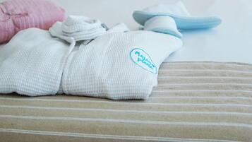Una cama bien tendida con almohadones a rayas, una bata doblada y pantuflas.