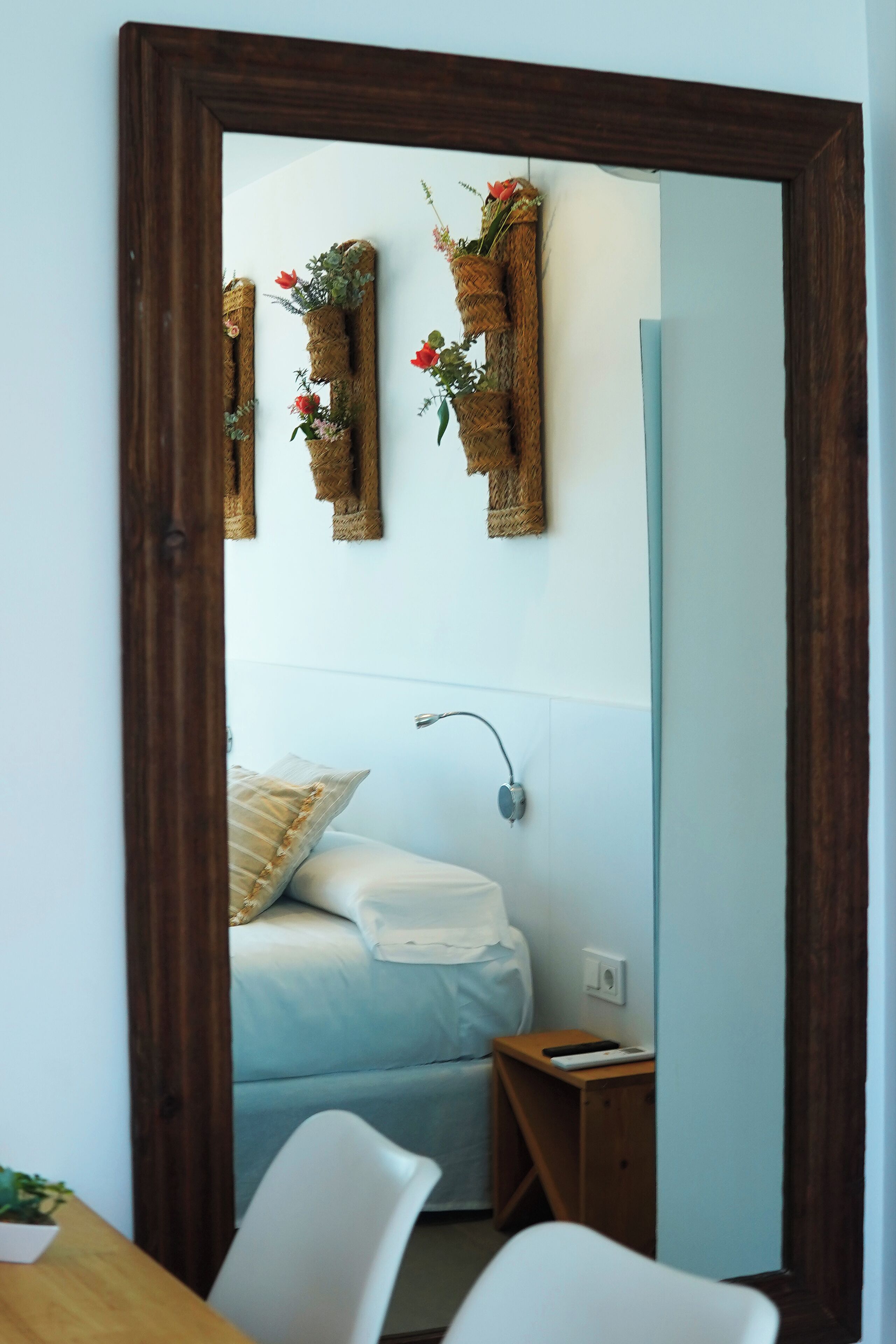 A bedroom with a bed, bedside table, and a mirror reflecting the room.