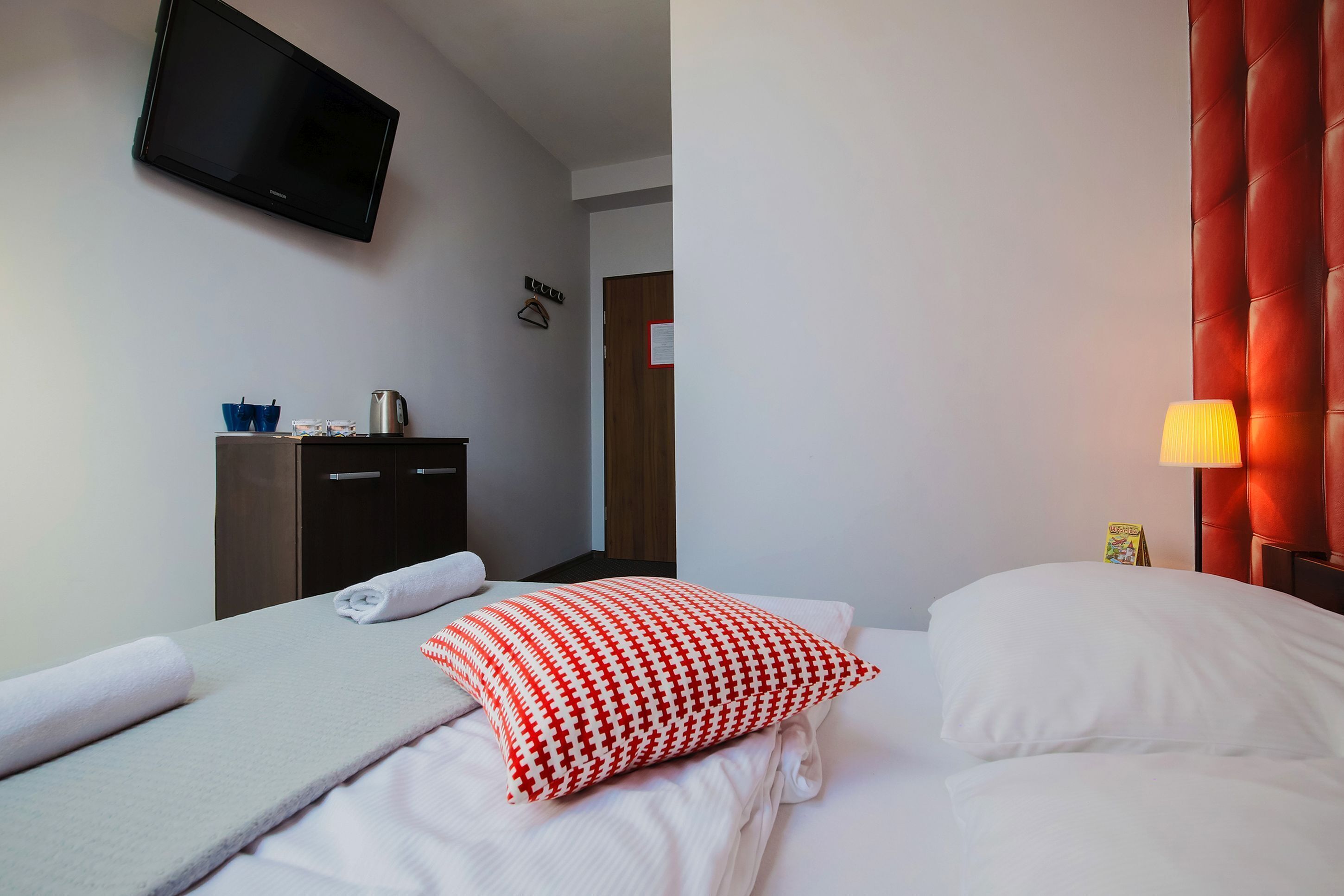 A hotel room with a bed, a TV mounted on the wall, a wardrobe, and a bedside table with a lamp.
