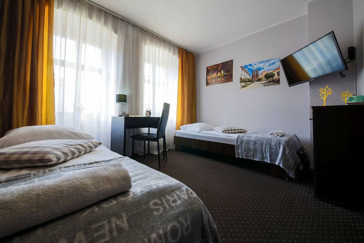 A hotel room with two beds, a desk, a chair, a television, and artwork on the wall.