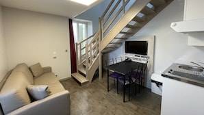 Un espacio habitable compacto con sofá, mesa de comedor, sillas, una pequeña cocina y una escalera.