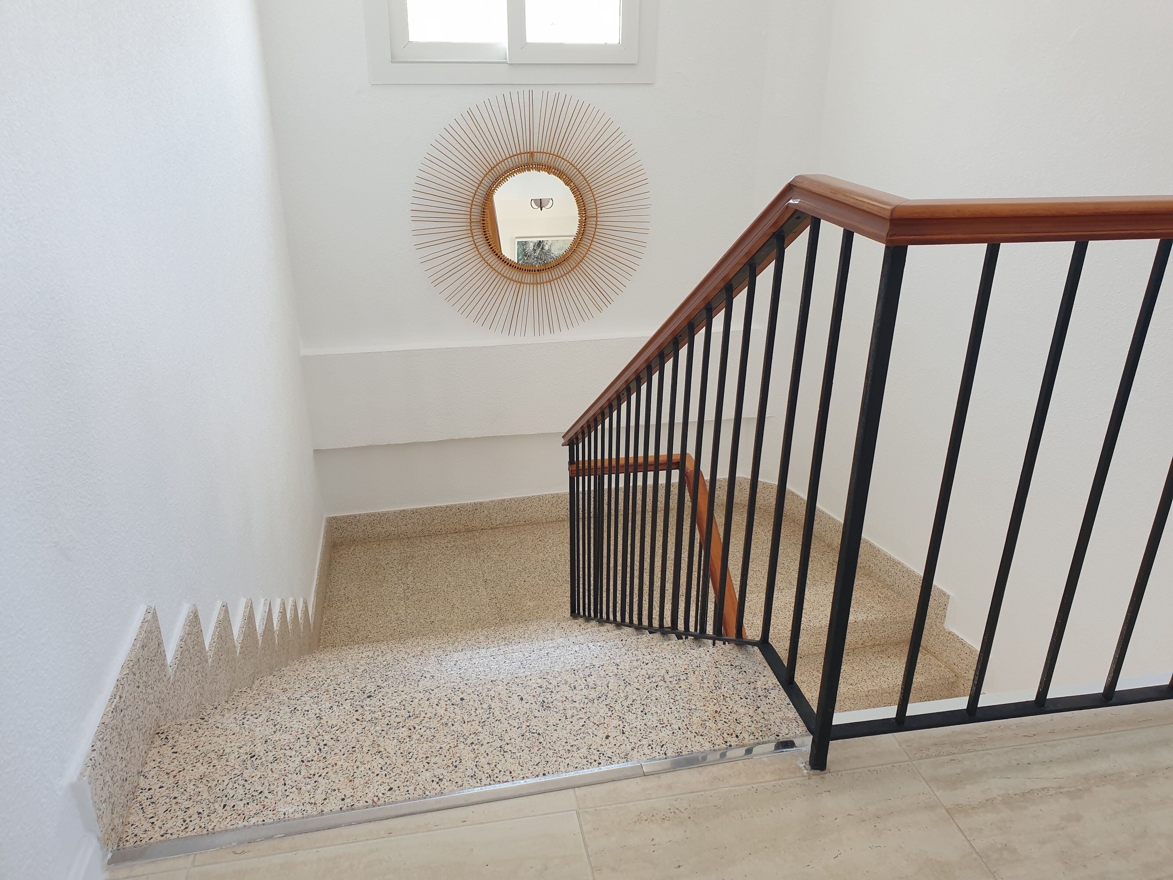 Una escalera con barandilla de madera y balaustres negros, que conduce a un rellano con un espejo decorativo en la pared.