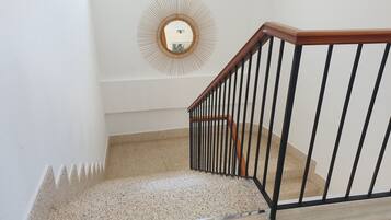 Una escalera con barandilla de madera y balaustres negros, que conduce a un rellano con un espejo decorativo en la pared.