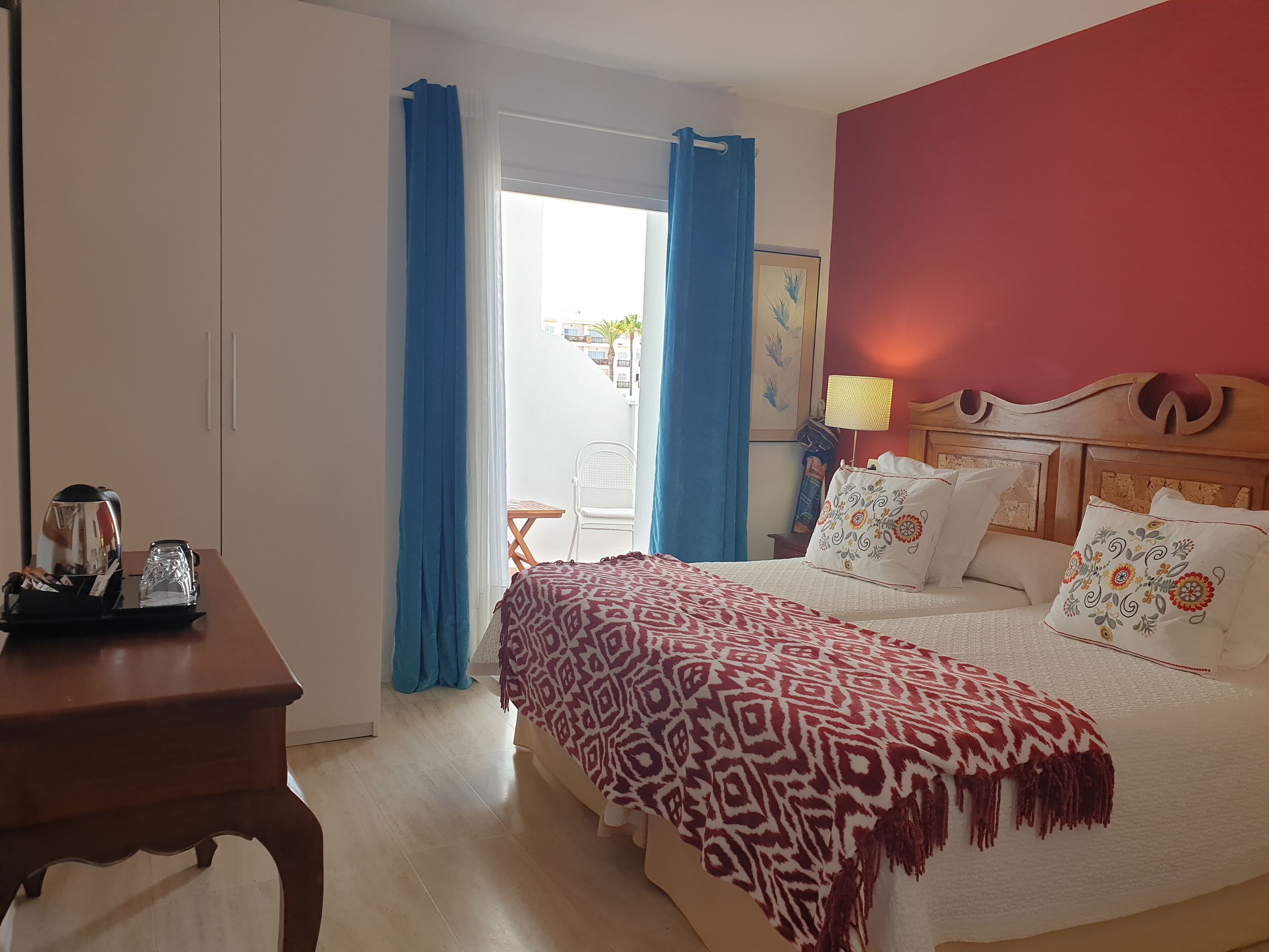 Una camera da letto con un letto, un comodino in legno, un tavolo con bollitore e bicchieri e vista all'esterno.