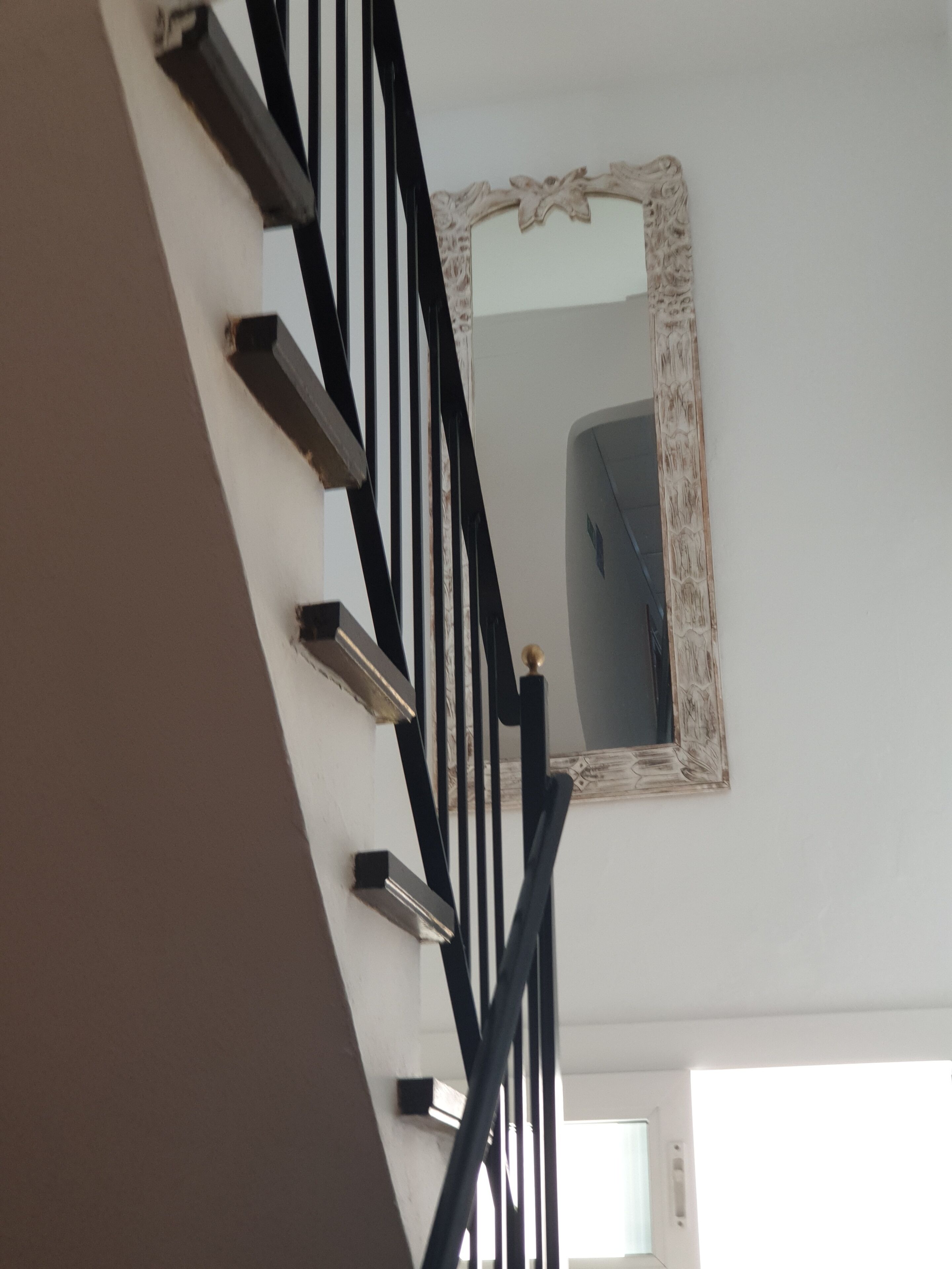 Una escalera con barandilla negra y un espejo decorativo en la pared.