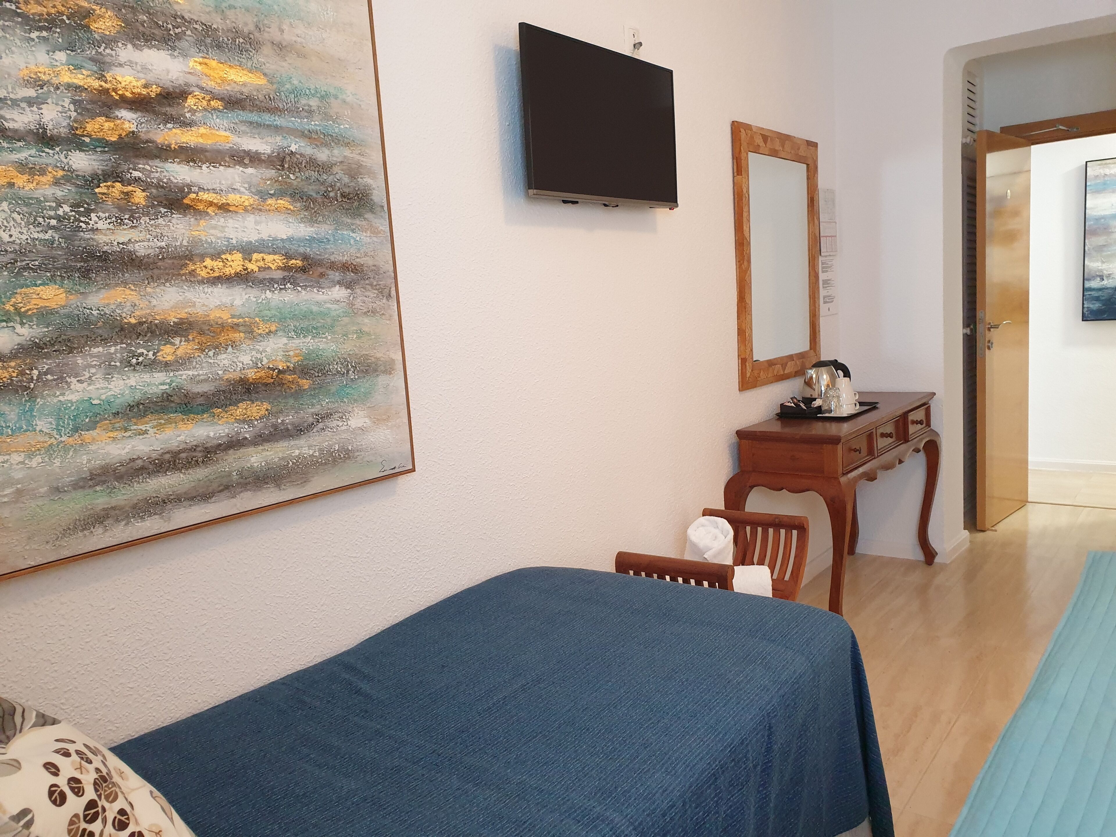 A bedroom with a bed, a painting, a television, a mirror, and a wooden dresser.