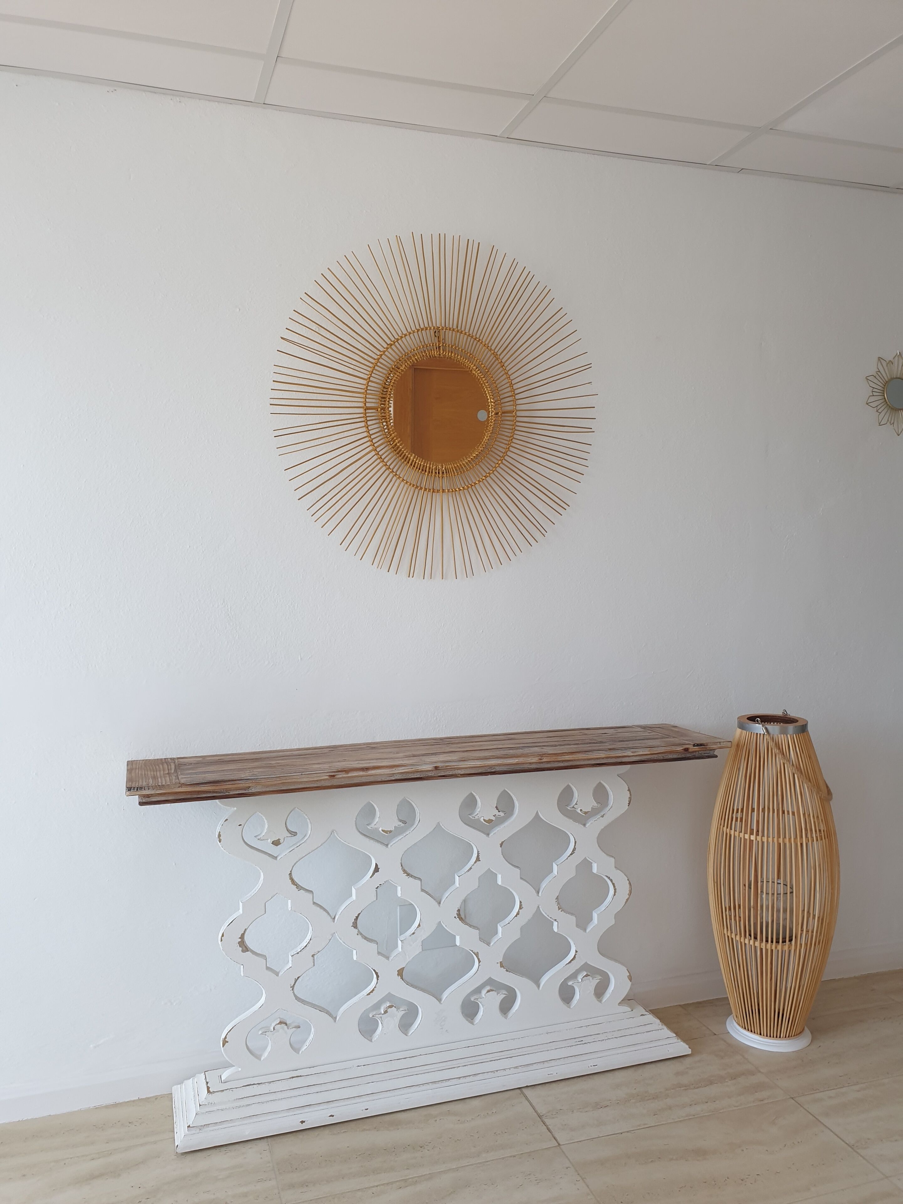 A room with a white wall, a wooden shelf, a decorative white panel, and a tall, slender vase.
