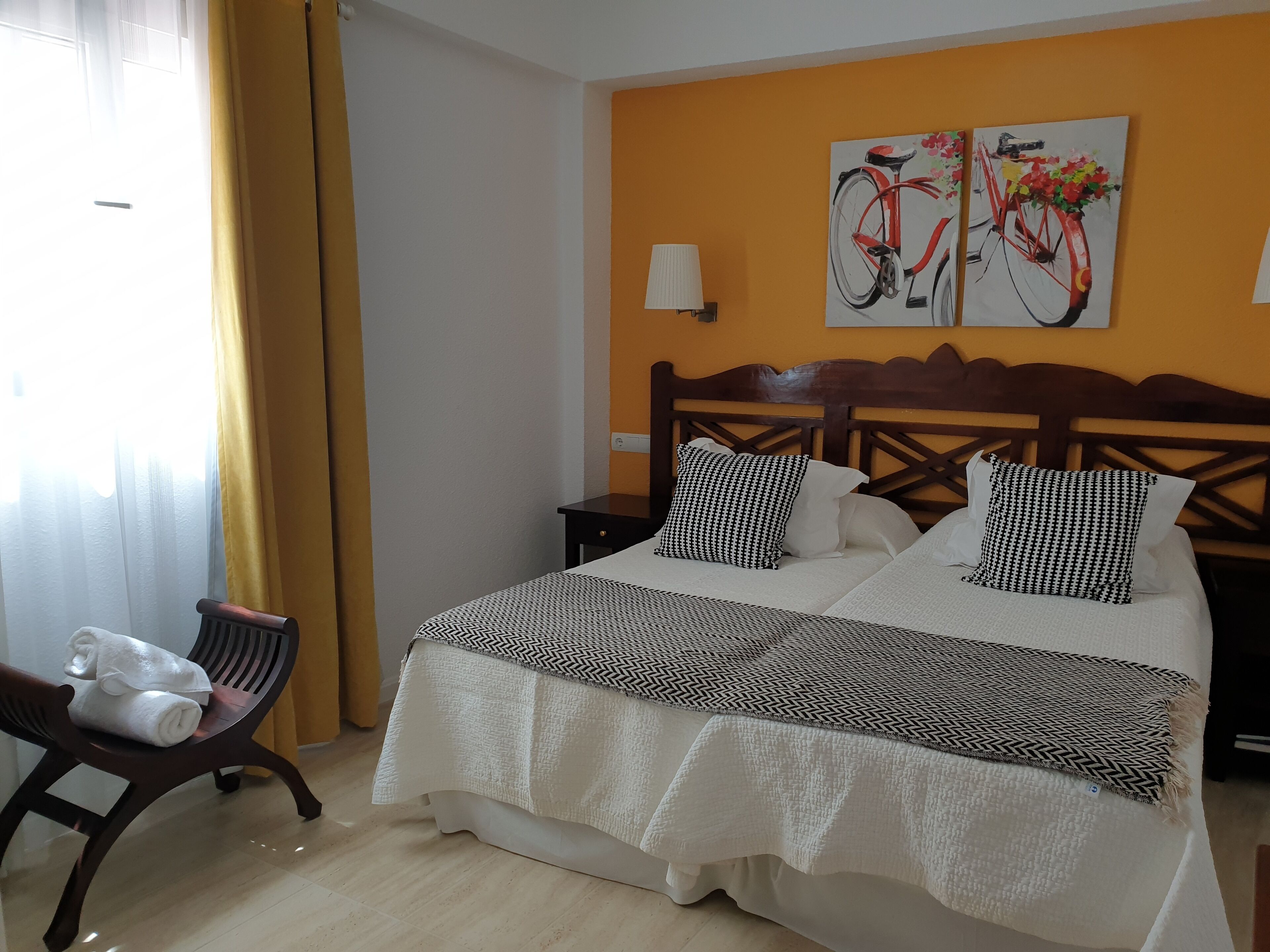 A hotel room with a bed, a chair, a nightstand, and two paintings on the wall.