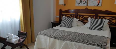 A hotel room with a bed, a chair, a nightstand, and two paintings on the wall.