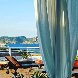 A terrace with a view of the sea and hills, featuring a table, chairs, and potted plants. - Hotel Boutique Las Arenas (Santa Eulalia del Rio)