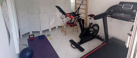 Une salle de sport à domicile équipée d’un tapis de course, d’un vélo d’appartement, d’un kettlebell, d’haltères et d’un tapis de yoga.