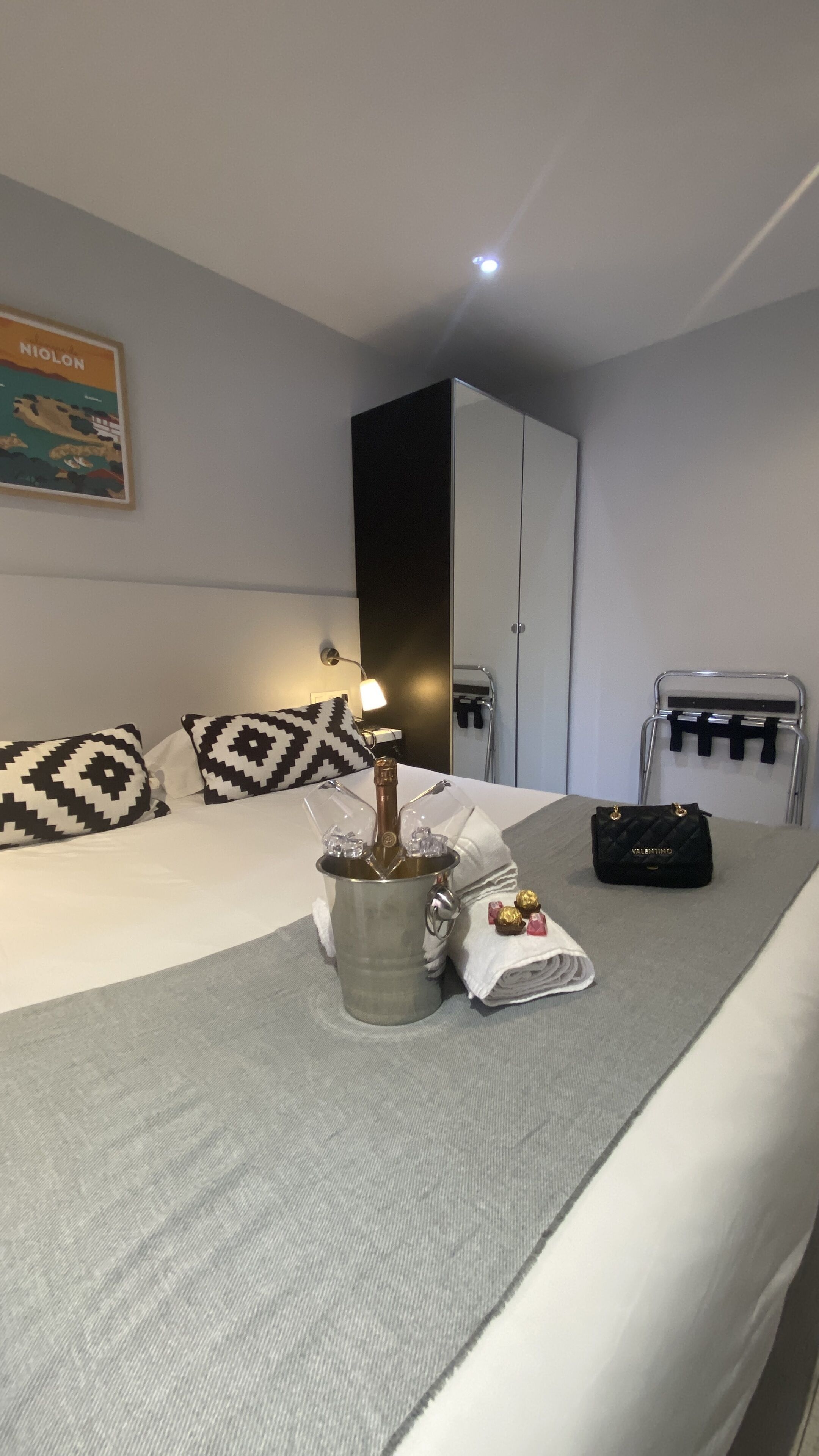 Une chambre d’hôtel avec un lit, un minibar, une valise et un porte-manteau.
