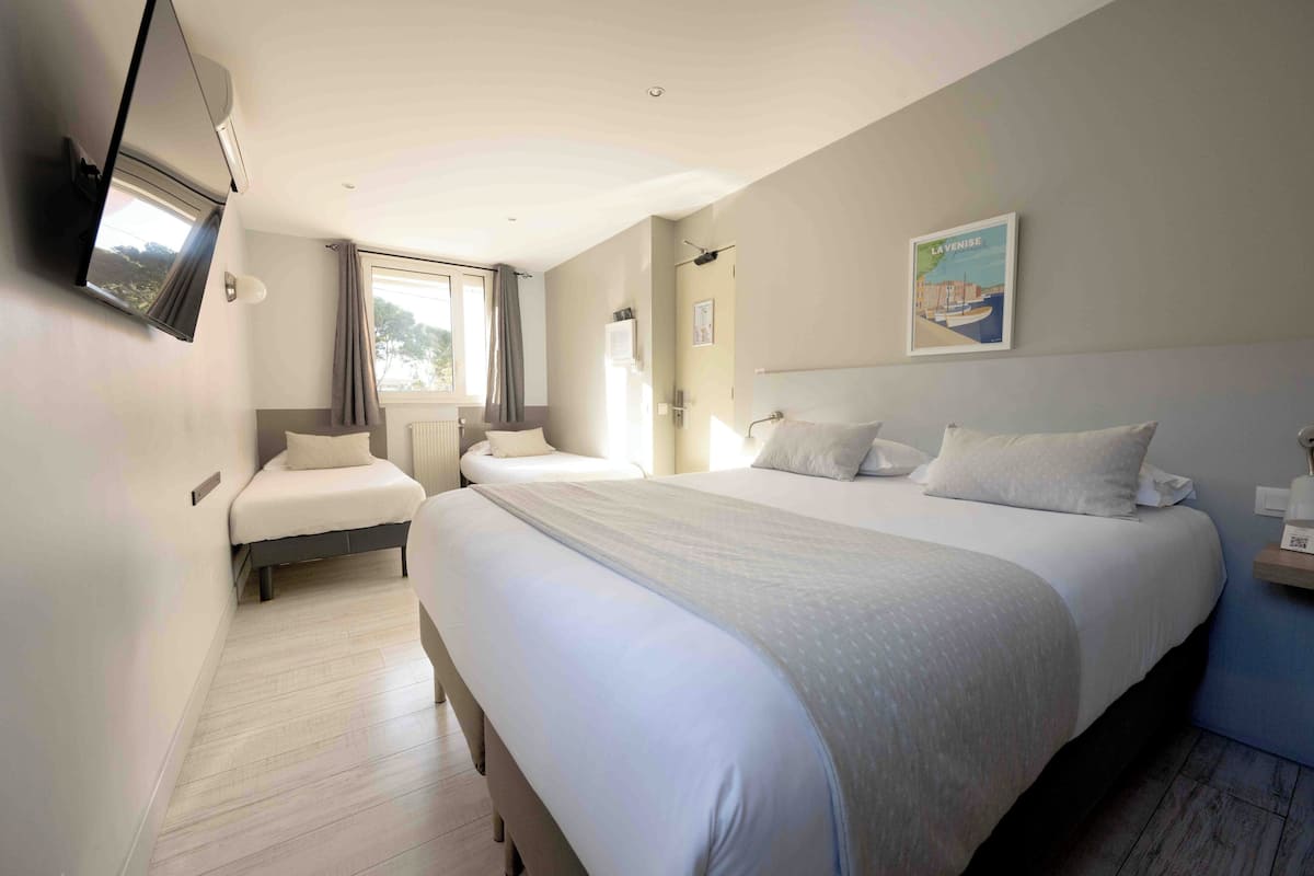 A hotel room with a large bed, a smaller sofa, a TV mounted on the wall, and a window with curtains.