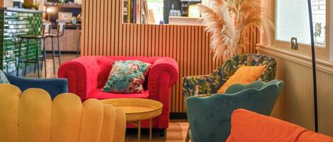 Una sala de estar acogedora con un sofá rojo, un sillón amarillo y un sillón azul con un cojín estampado.