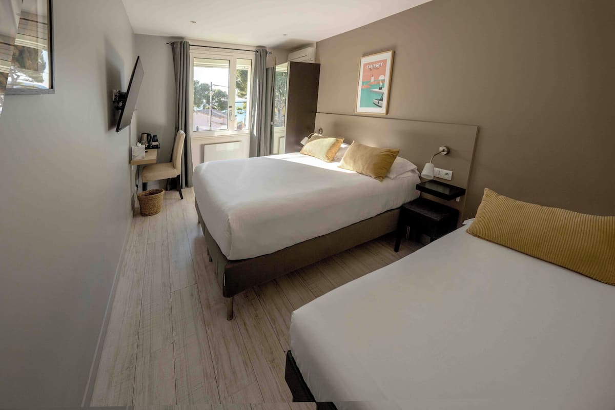 A hotel room with a large bed, a bedside table, a chair, a TV mounted on the wall, and a window with curtains.