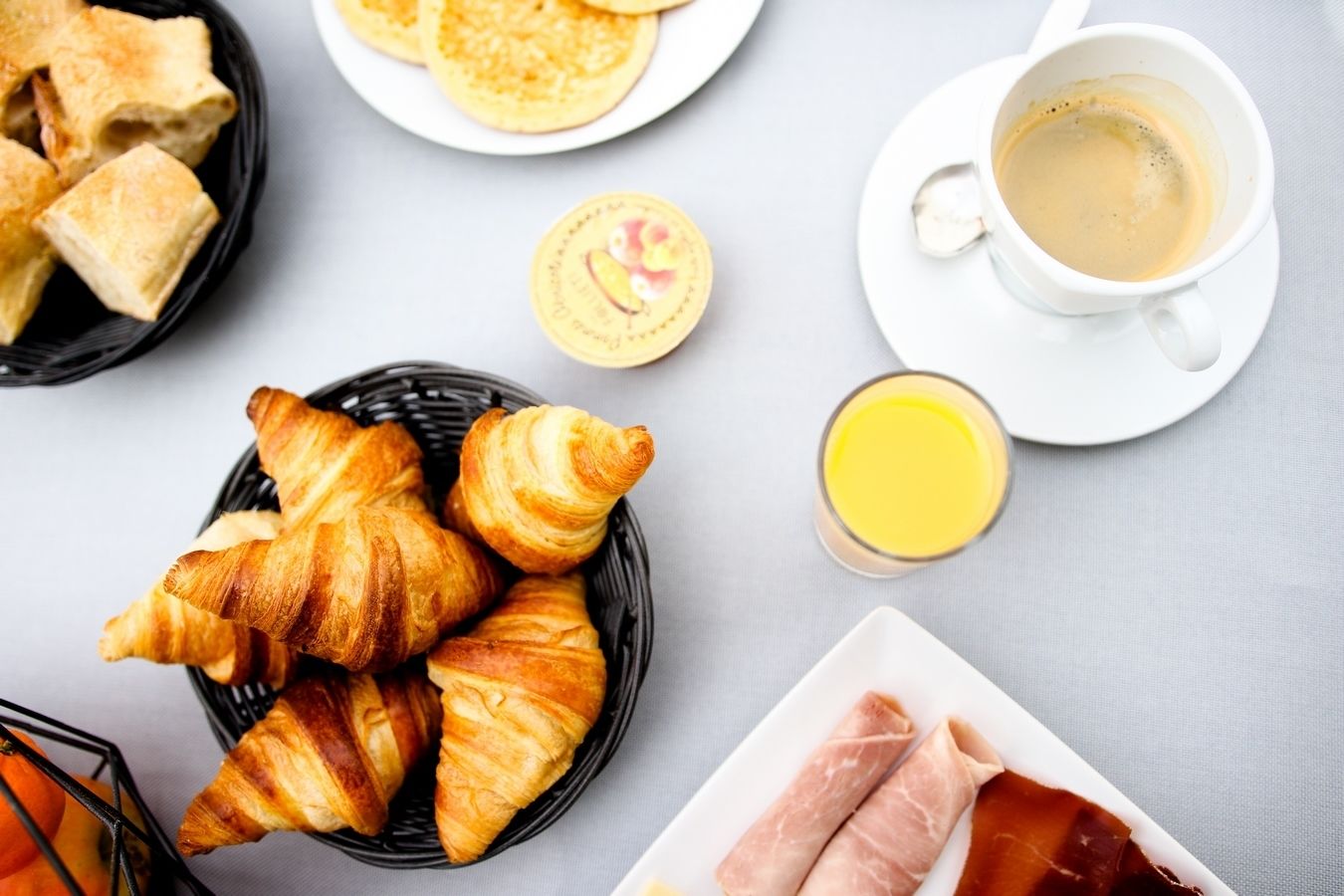A breakfast setting with croissants, pancakes, coffee, juice, and meat.