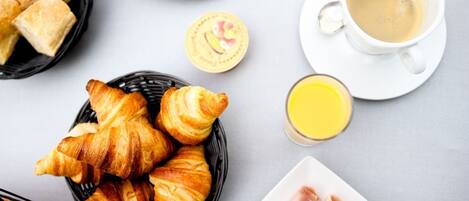 Un petit-déjeuner composé de croissants, de crêpes, de café, de jus de fruits et de viande.