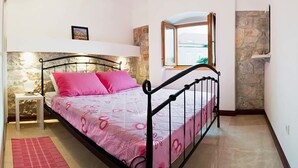 Une chambre à coucher avec un lit, une table de chevet, un tapis rouge, un mur en pierre et une fenêtre donnant sur un beau paysage.