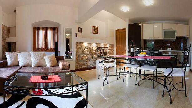 Un salon moderne avec une table basse en verre, un canapé agrémenté de coussins à motifs et un coin repas comprenant une table avec un plateau en verre et des chaises en métal.