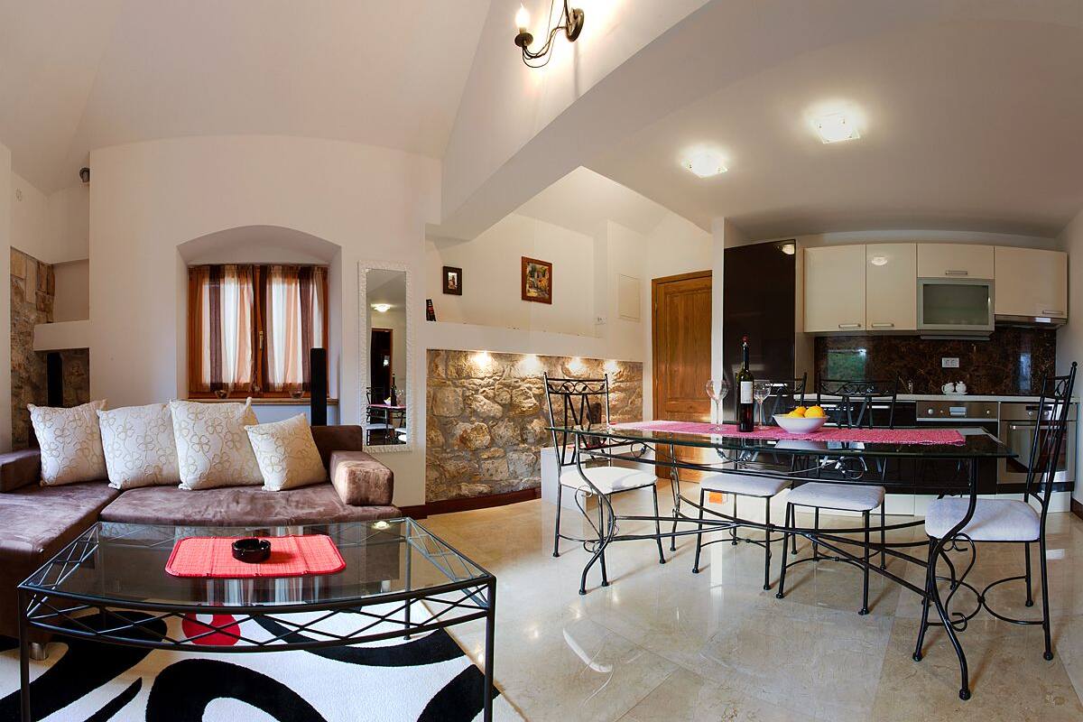 A modern living room with a glass coffee table, a sofa with patterned cushions, and a dining area with a glass-top table and metal chairs.