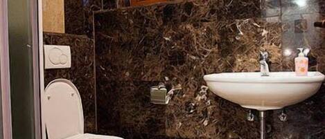 A bathroom with a marble wall, a white sink, and a toilet.