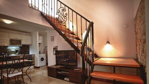 Un salon avec un escalier en bois, un coin repas avec une table et des chaises, et une cuisine à l’arrière-plan.