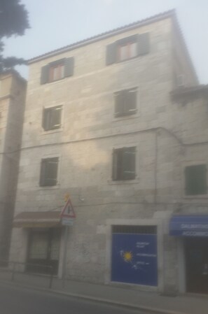 Um edifício de vários andares com fachada de pedra, diversas janelas e uma placa azul com texto.
