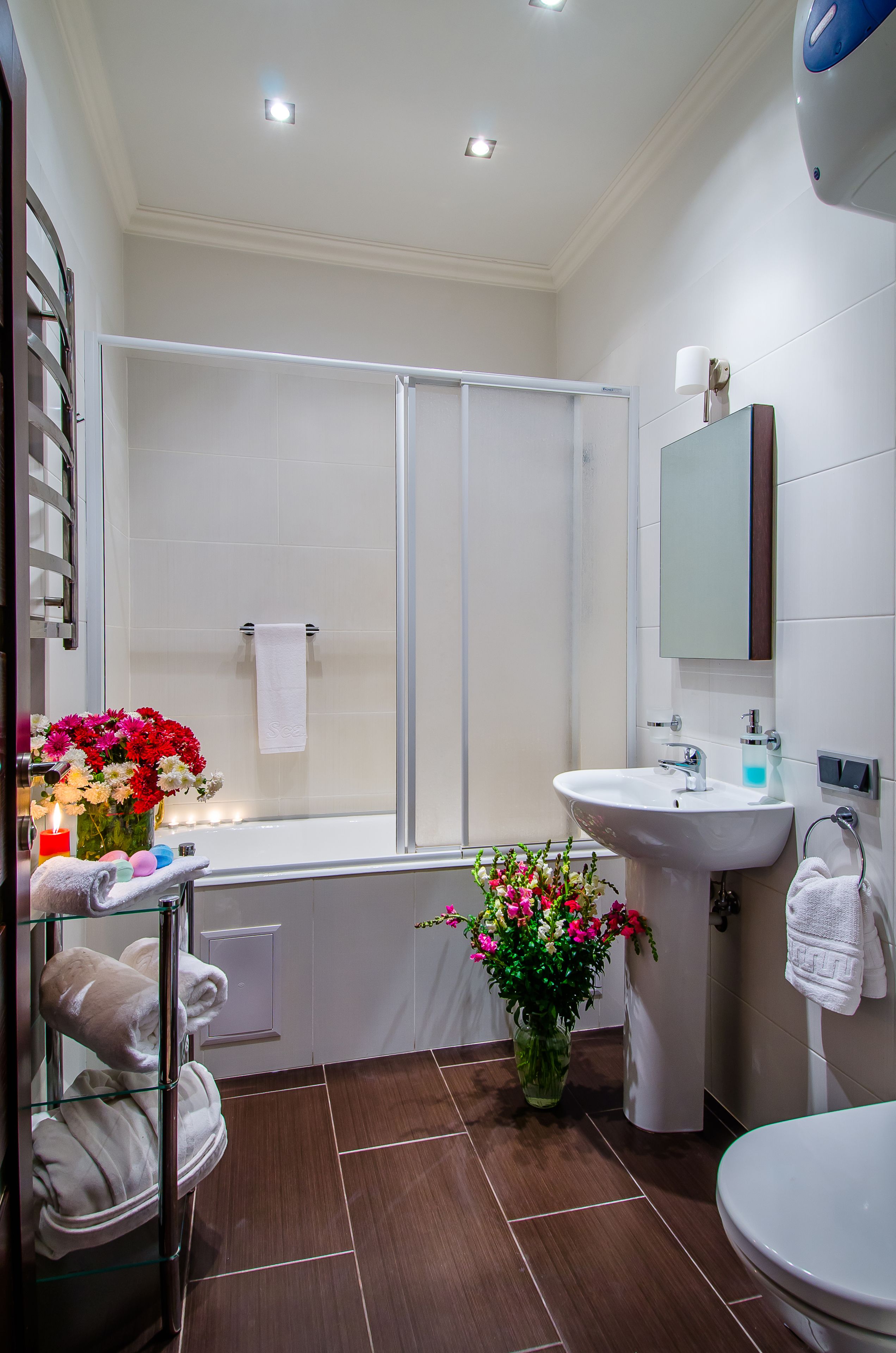 Un baño moderno con una bañera, un lavamanos y un inodoro. Hay un perchero con toallas y un jarrón con flores.