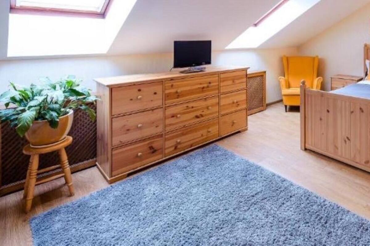 Quarto com cama de madeira, cómoda, cadeira e televisão.