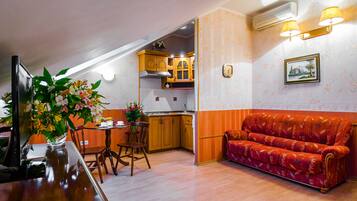 A cozy kitchen with wooden cabinets, a dining table with chairs, and a red sofa.