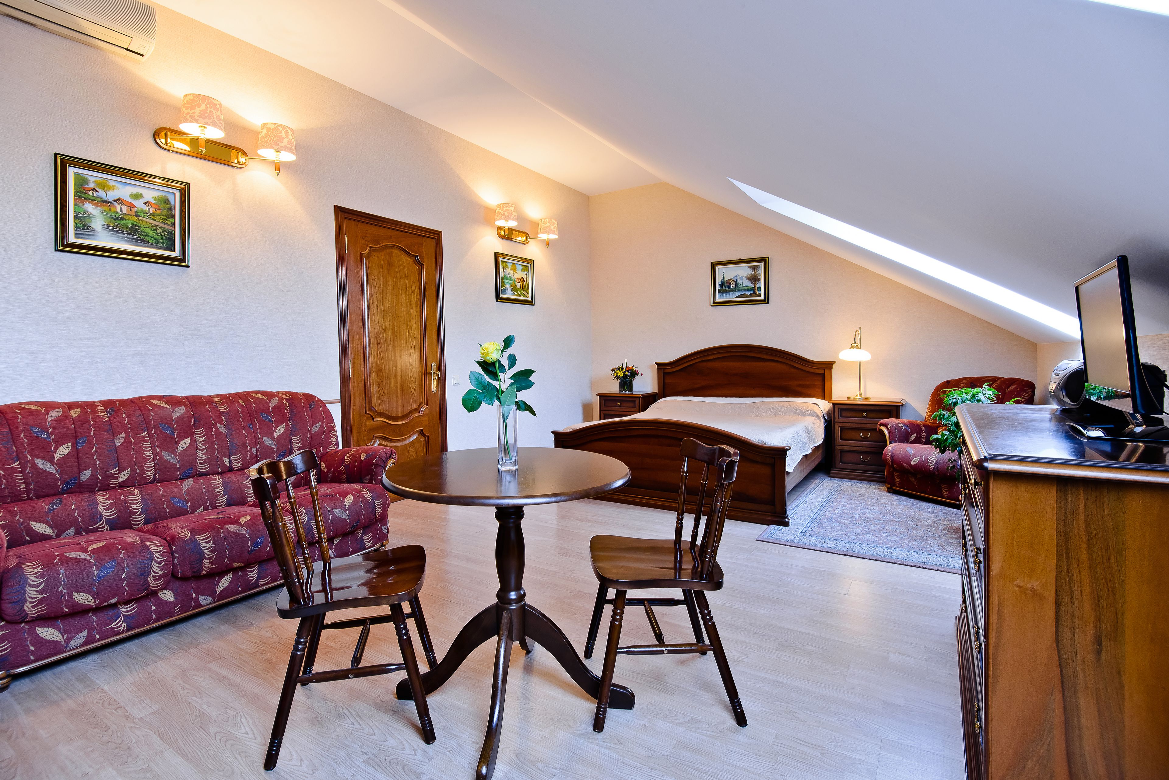 Une pièce chaleureuse avec une table ronde en bois, deux chaises, un canapé, un lit et un bureau avec un ordinateur.