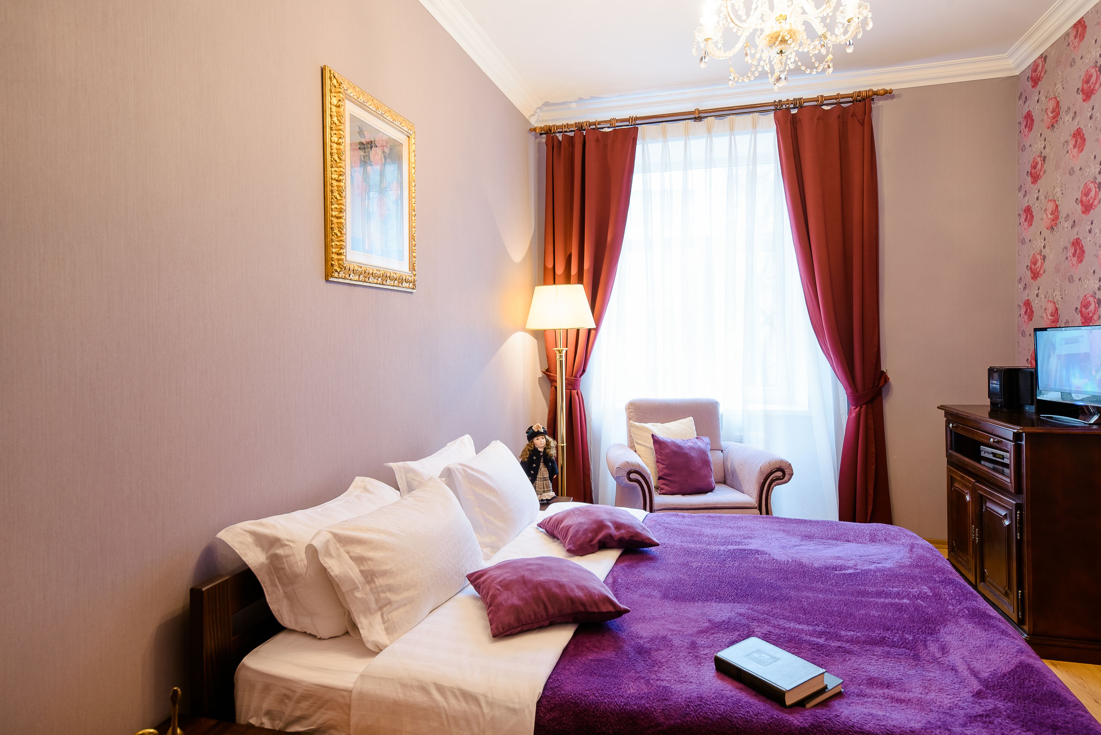 A hotel room with a bed, a chair, a desk with a television, and a window with curtains.