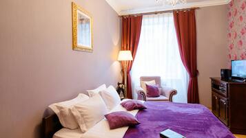 A hotel room with a bed, a chair, a desk with a television, and a window with curtains.