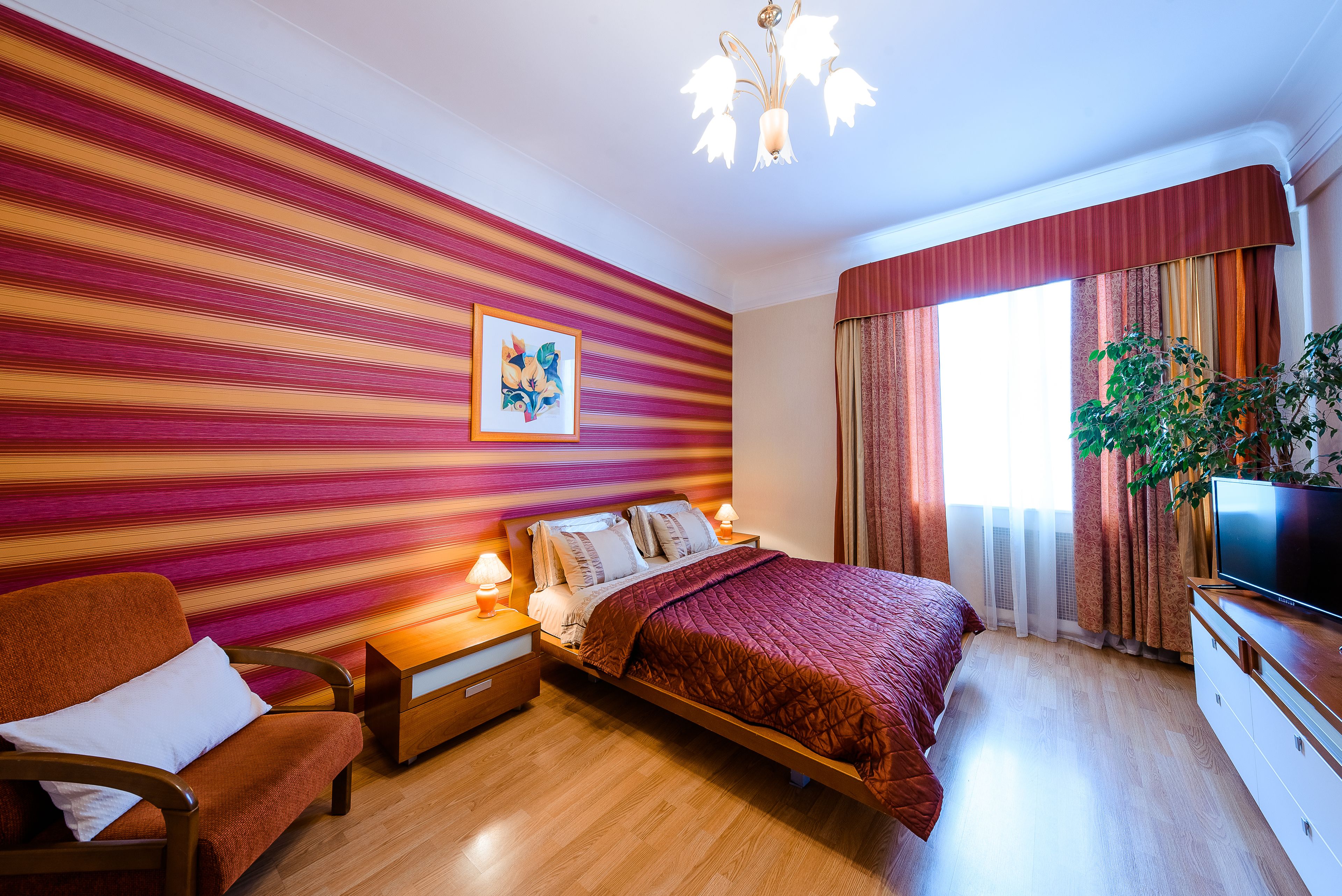 Une chambre moderne avec un mur à rayures, un lit, une chaise, une table de chevet, un téléviseur et une fenêtre avec des rideaux.