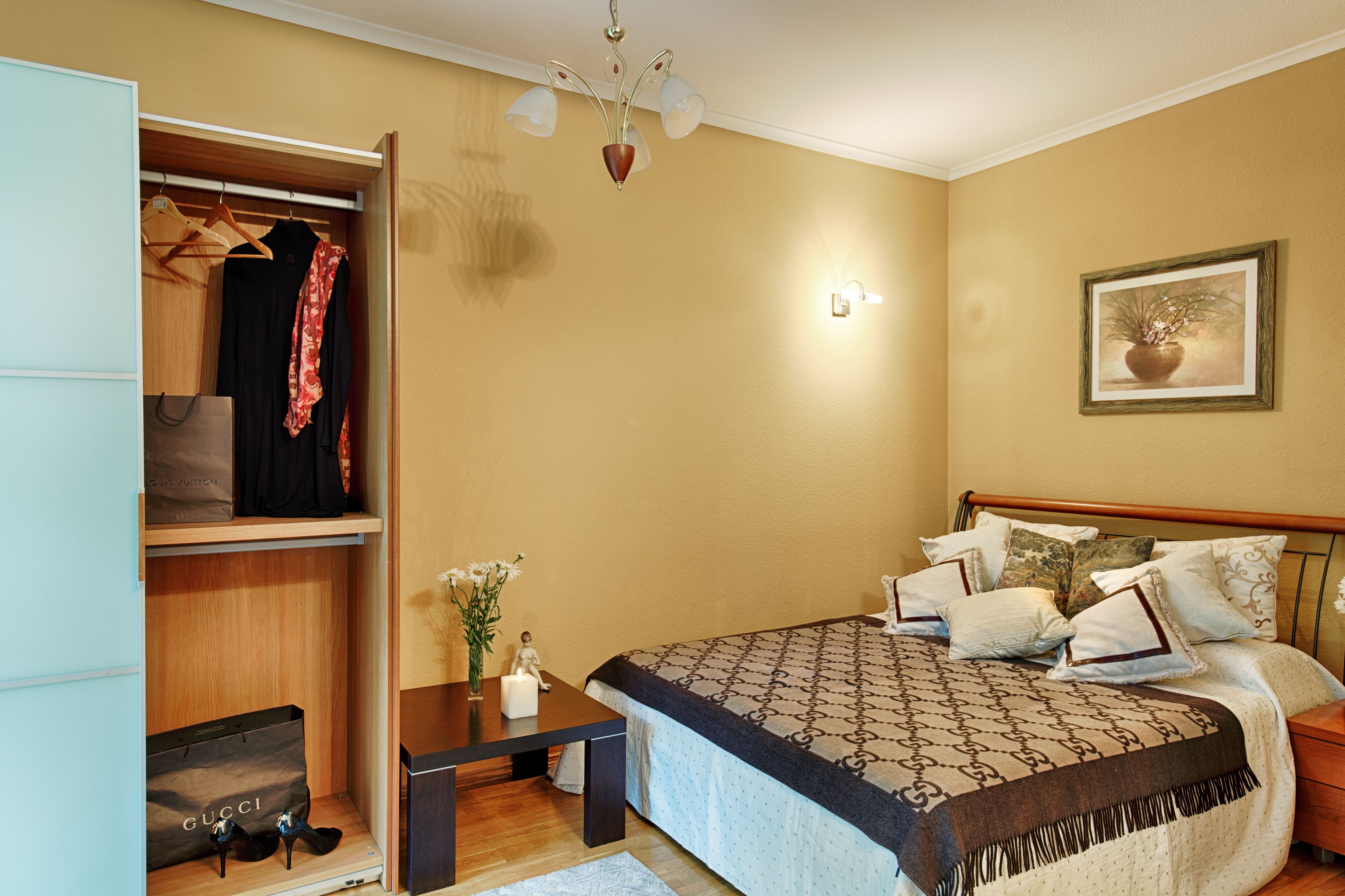 A bedroom with a bed, bedside table, nightstand, wardrobe, and a painting on the wall.