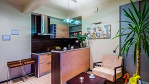 A modern kitchen with a built-in oven, a dining area with a wooden table and chairs, and a large potted plant. - Sherborne ApartHotel (Kyiv)