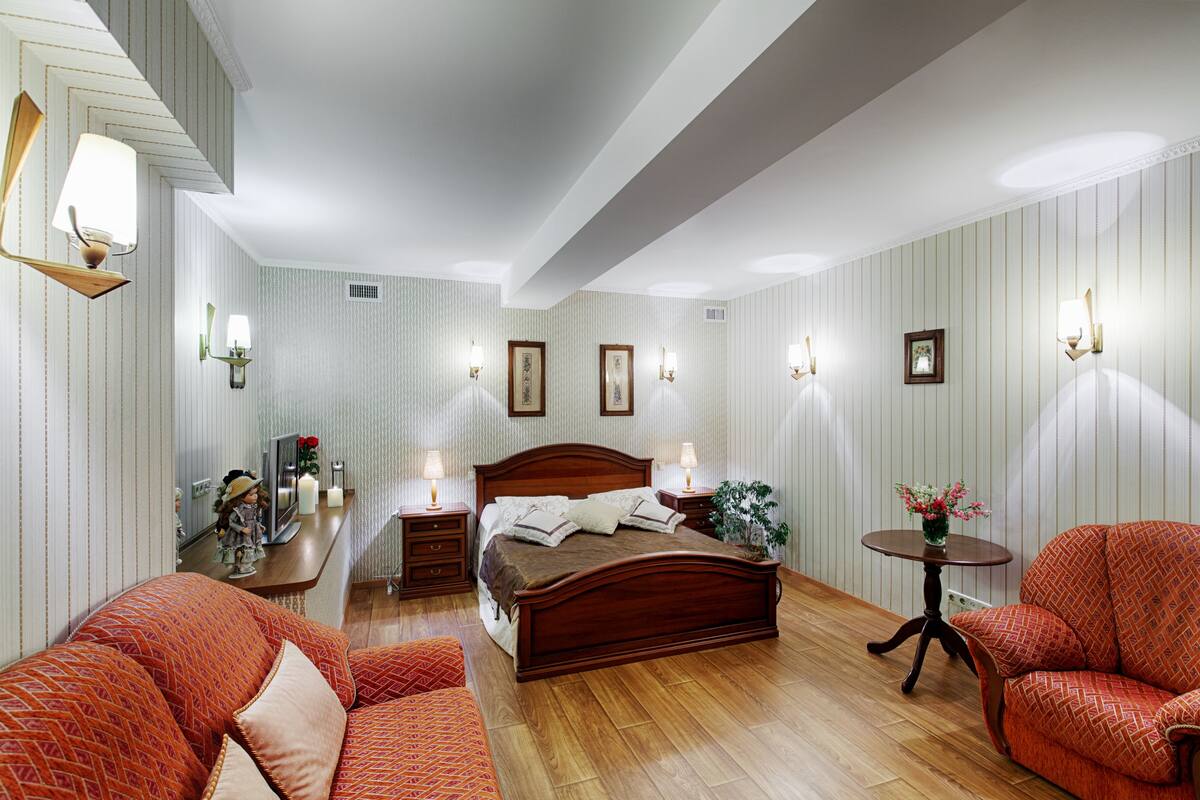 Quarto com cama de madeira, uma mesinha com um vaso e duas cadeiras.