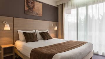 Una camera d'albergo con un letto grande, due comodini con lampade, una testiera in legno, un dipinto di Buddha e un'ampia finestra con tende.