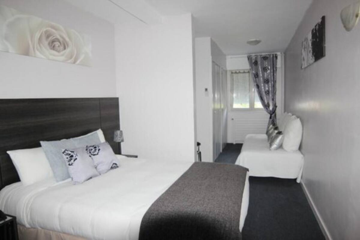 A hotel room with a bed, a chair, a large white wall with a rose decoration, and a window with curtains.