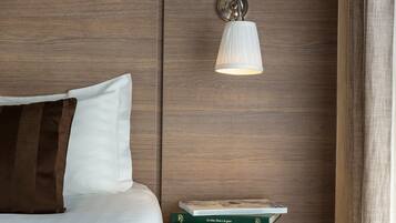 A neatly made bed with a white and brown pillow, a small bedside table with a book, and a wall-mounted light fixture.
