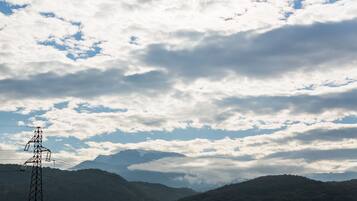 A power line tower amidst a mountainous landscape with a partly cloudy sky.