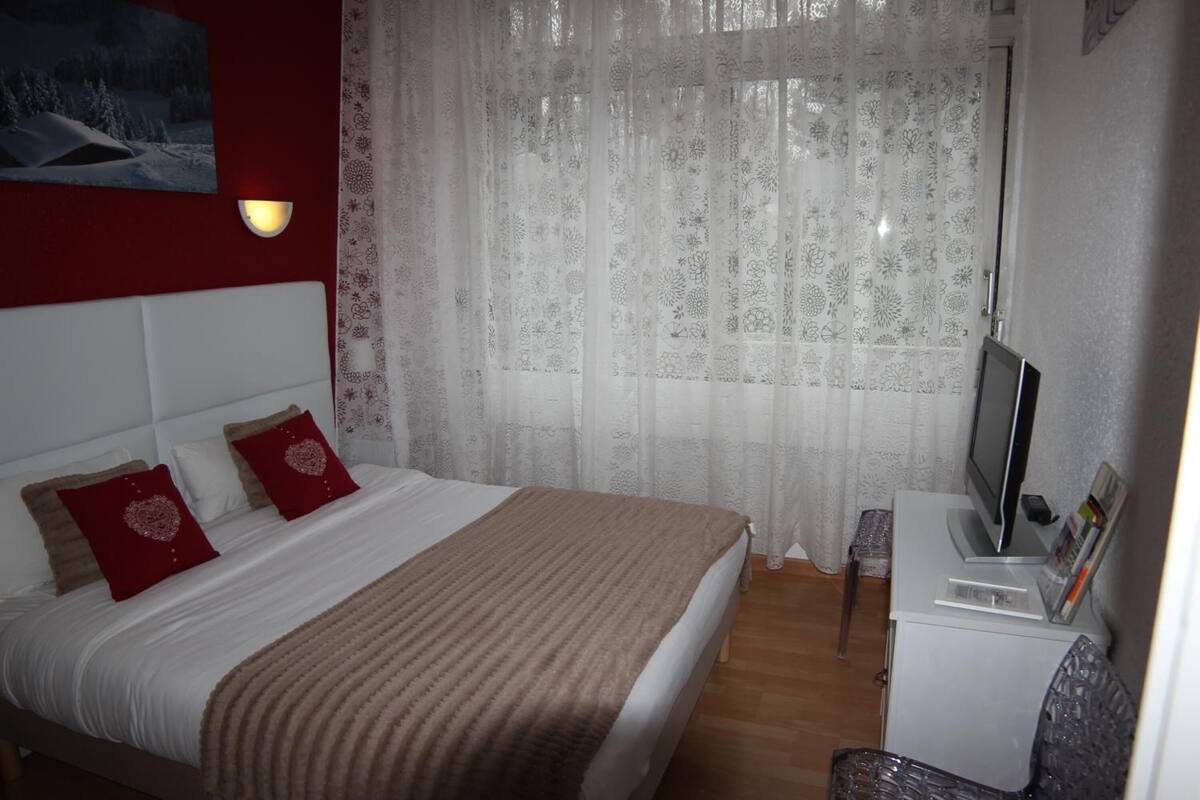 A neatly made bed with a white headboard, two red pillows, and a brown blanket. A television is on a small table beside the bed.