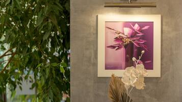 A framed artwork of pink flowers on a wall, a vase with white flowers, and green foliage.