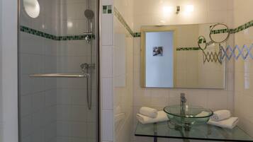 Un baño con lavamanos de vidrio, ducha con cerramiento de vidrio y espejo con marco decorativo.