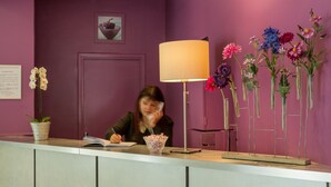 En receptionsdisk med en kvinna sittande bakom den, en lampa och olika blomsterarrangemang.