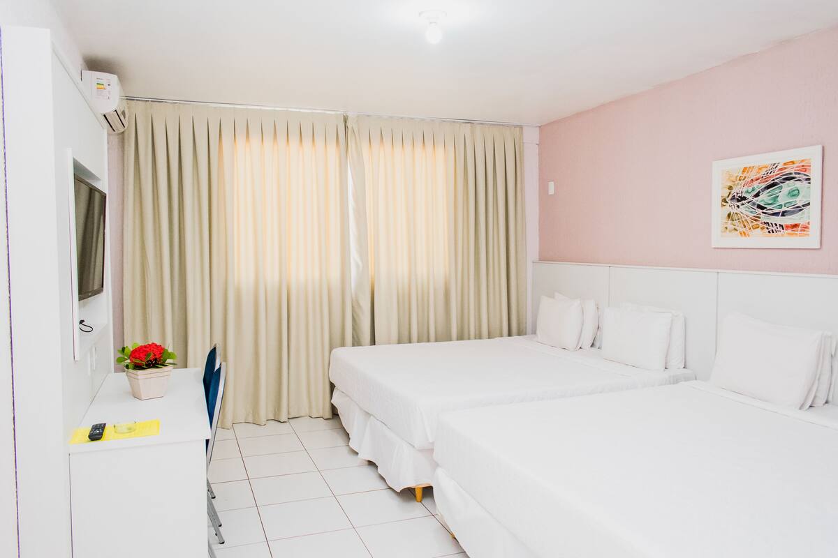 A hotel room with a bed, a desk, a TV, and a window with curtains.