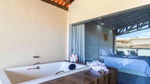 A modern bathroom with a large bathtub, wooden vanity, and a view of a bedroom with a bed and a balcony. - Nauticomar Resort All Inclusive & Beach Club (Porto Seguro)